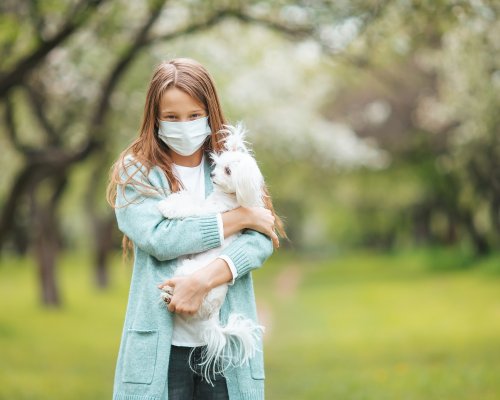 Little girl wearing a protective mask is walking alone with a dog outdoors because of the coronavirus pandemic